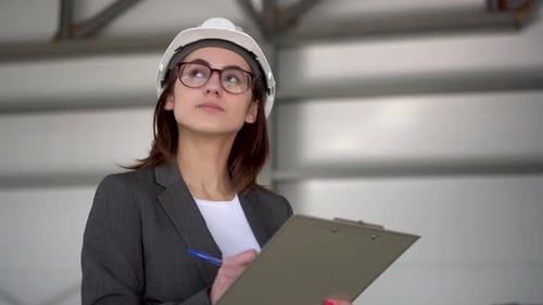 Young Woman in a Helmet with Documents at a Construction Site. The Boss Woman in a Suit Keeps