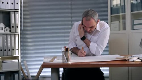 Man on Phone Drawing on Blueprints in Office