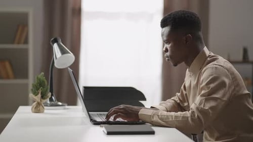 Young Black Man is Working Remotely From Home Freelancer is Surfing Internet in Notebook Looking