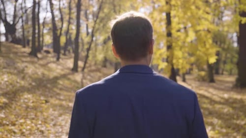 A Middleaged Handsome Caucasian Man Walks and Looks Around in a Park in Fall Rear Closeup
