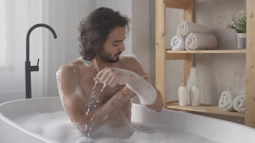 Young Man in Tub Washing with Yellow Sponge