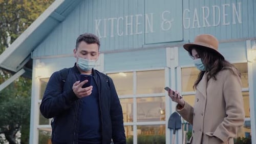 Masked Man and Woman with Smartphones Outside Store