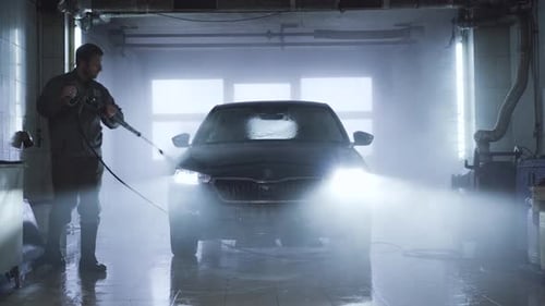 Adult Confident Caucasian Man Washing Vehicle in Auto Care Shop. Professional Washer Cleaning Car