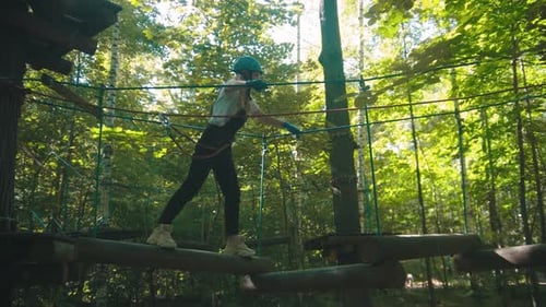Young Woman on an Attraction in the Park - Walking on the Logs Hanging on Ropes
