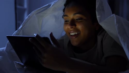 Woman with Tablet Pc Under Blanket in Bed at Night