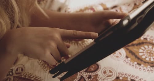 Blonde Woman Uses Tablet While Lying on Bed