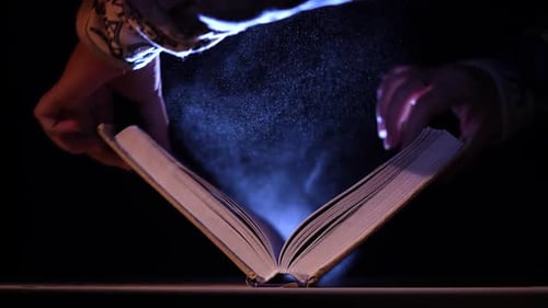 An Open Book Lies on a Table in a Dark Studio Under the Spotlight