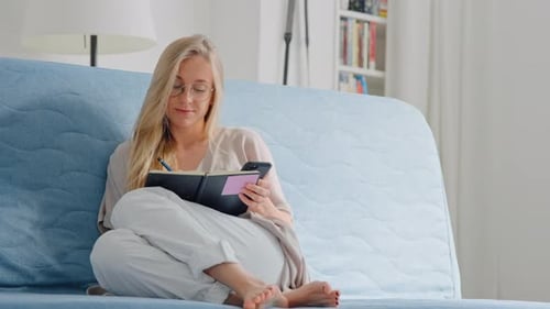 Woman on Couch Using Phone and Writing
