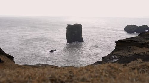 Rocky cliff washed by foamy sea in overcast weather