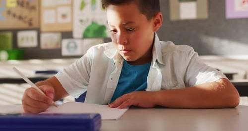 Young Boy Writes at Desk in Classroom