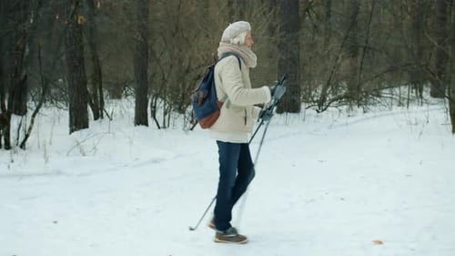 Side View of Elderly Woman Walking in Forest with Ski Poles Busy with Winter Sports Outdoors