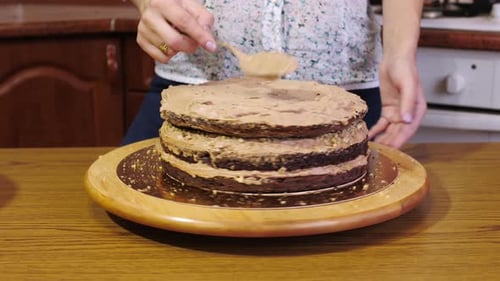 Woman Frosting Multi-Layered Chocolate Cake in Kitchen