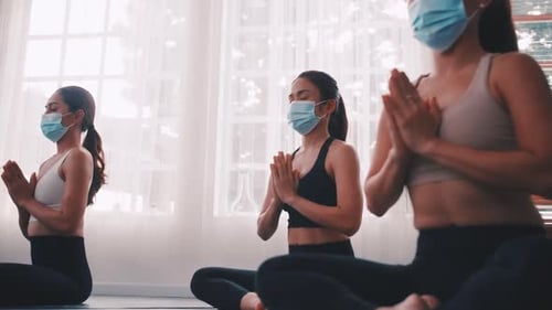 Um grupo de mulheres asiáticas usando máscaras médicas enquanto fazem exercícios de ioga na academia.
