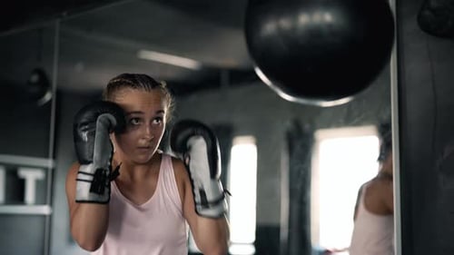 A Muscular Alone Woman is Hits Punching Bag in the Gym