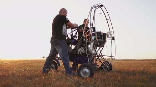 Motor-Gleitschirm steht bei Sonnenuntergang mit einem Holzpropeller auf dem Feld, zwei Piloten