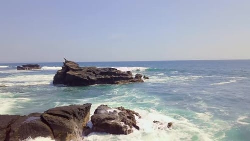 Aerial View Over a Rocky Seashore and Wavy Blue Ocean. White Waves Crashing.