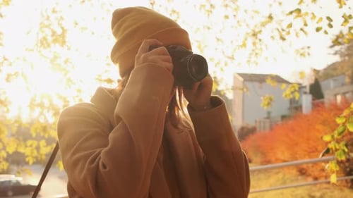 The Camera Pans Around a Young Woman Photographer Taking a Photo at Sunset in an Autumn Park