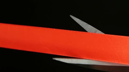 On a Black Background Cut Red Ribbon Scissors. Slow Motion