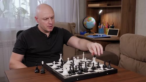 Ein erwachsener Mann spielt zu Hause Schach mit sich selbst und sitzt am Tisch