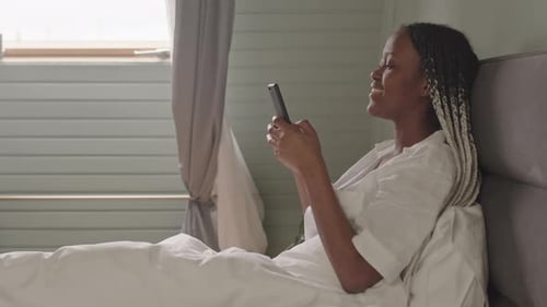 Young Black Woman Texting on Smartphone in Bed