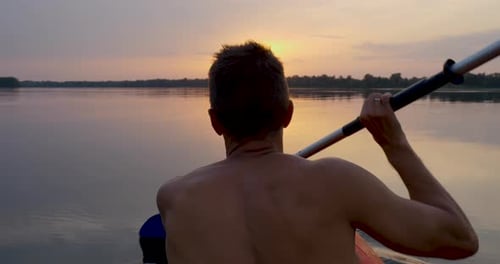 A Man Kayaks on a Calm River Towards the Sunset