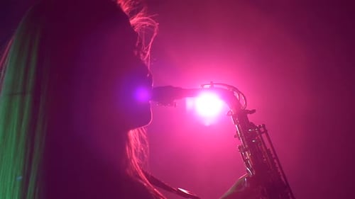Woman Playing Saxophone in Pink and Green Lighting