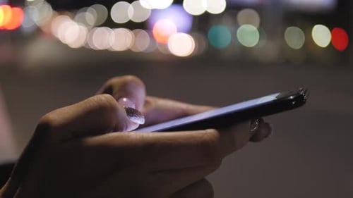 Close Up Woman Using Smartphone in the City at Night Time. Girl Looks at the Smartphone Screen