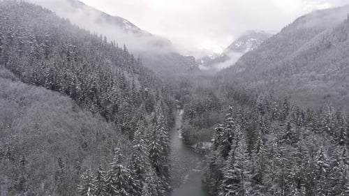 4k Helicopter View Of Gray Fog On Forest Mountain Tops With Snow Flakes Falling In Valley River