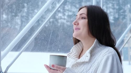 Woman Enjoys Hot Drink Looking at Winter in Panoramic Window