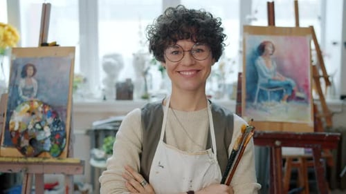 Portrait of Young Female Painter Standing in Modern Painting Studio Holding Brushes