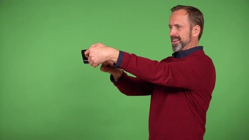 A Middleaged Handsome Caucasian Man Takes Selfies with a Smartphone Green Screen Background
