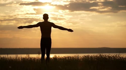 Silhouette of Young Sportive Man Practicing Yoga at Sunset