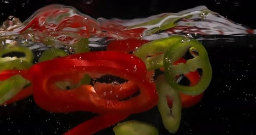 Slices of Peppers Fall Down Into Water and Float on Surface