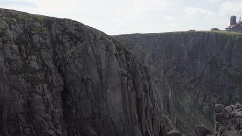 A View of Tall Rocky Mountains, One House Stands on the Other Side of the Mountain