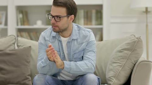 Man Sitting on Couch Rubbing Hands Thoughtfully