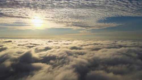 Aerial view of vibrant yellow sunrise over white dense clouds with blue sky overhead.