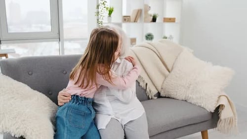 Child Hugs Senior Woman on Gray Couch