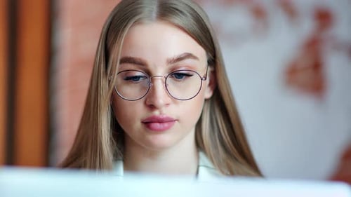 Nahaufnahme einer schönen, vielbeschäftigten jungen Geschäftsfrau mit Brille, die auf den Bildschirm eines Laptops schaut