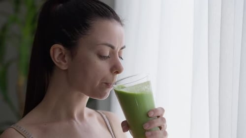 Woman Enjoying Healthy Green Smoothie By Window