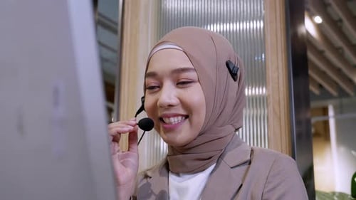 Beautiful woman in hijab at the computer with headset, distant work, call center