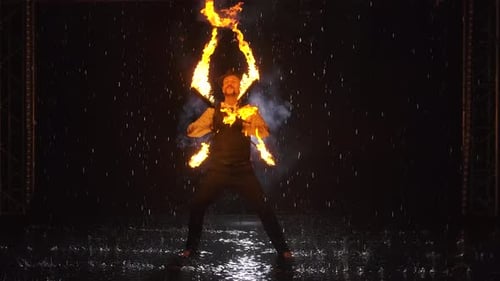 Silhouette of a Man Doing a Professional Fire Show in a Dark Studio in the Rain. Slow Motion