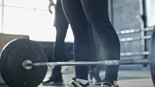 Determined Woman Deadlifting with Trainer Supervision in Gym