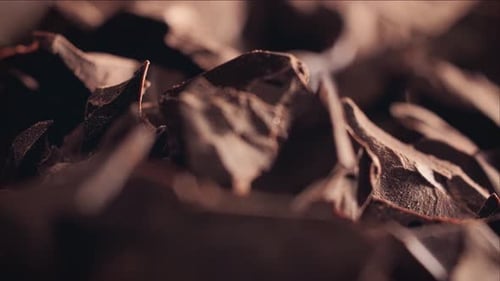 Chunks of sweet dark chocolate sliding backdrop, close-up. Gourmet dessert ingredient.