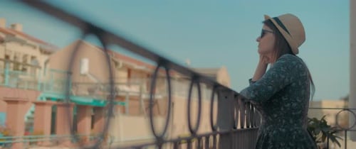 Woman Stands on Balcony Overlooking City on Sunny Day