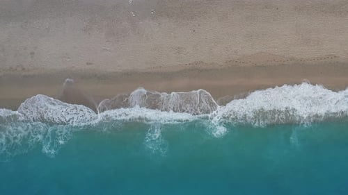 Statische Ansicht von oben nach unten auf Sandstrand und türkisfarbene Meereswellen am Uferrand