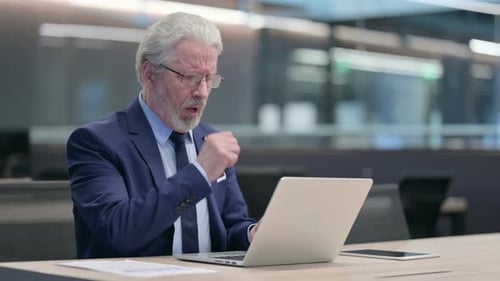 Mature Businessman Coughing While Using Laptop in Office