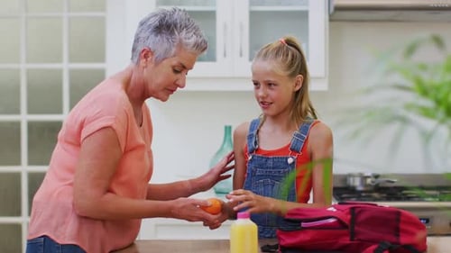 Grandmother Helping Granddaughter Pack Lunch in Kitchen