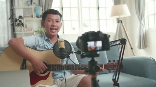 Un chico asiático es un vlogger. Chico con guitarra hablando con la cámara. El chico está transmitiendo