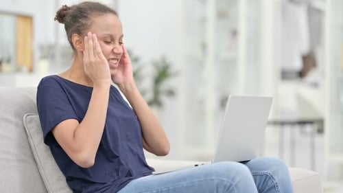 Young Woman Typing on Laptop Holds Her Head
