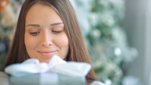 Smiling Woman Holds Christmas Present by Christmas Tree
